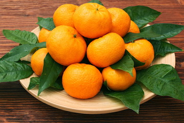 Ripe orange tangerines with green leaves in plate