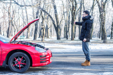  Man signaling problems with broken sport car on winter road.