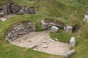 Orkneys, Scotland - June 5, 2012: Skara Brae Neolithic Settlement. Group of ruins and fundaments of dwelling, set in the green dunes. Gray and brown stones. Sandy patches.
