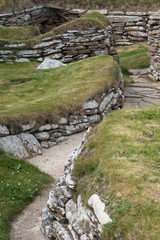 Orkneys, Scotland - June 5, 2012: Skara Brae Neolithic Settlement. Group of ruins and fundaments of dwelling, set in the green dunes. Walls and walkways. Gray and brown stones.