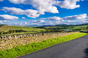 View on farms and countryside road, tarmac road, Summer, blue sky and white clouds, Forest Of Bowland, Lancashire, England, UK