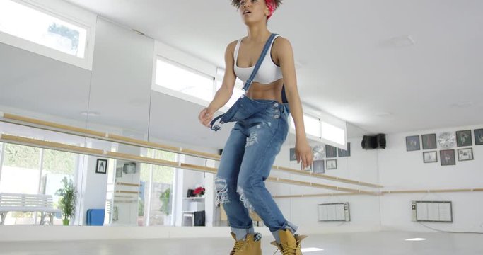 Woman in work boots and overalls dancing in a studio as seen from a low angle view