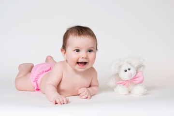 Little girl smiling with a toy rabbit lies on white background.