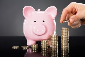 Person Stacking Coins In Front Of Piggybank