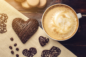 Coffee cappuccino with beautiful foam next macarons and chocolate heart.