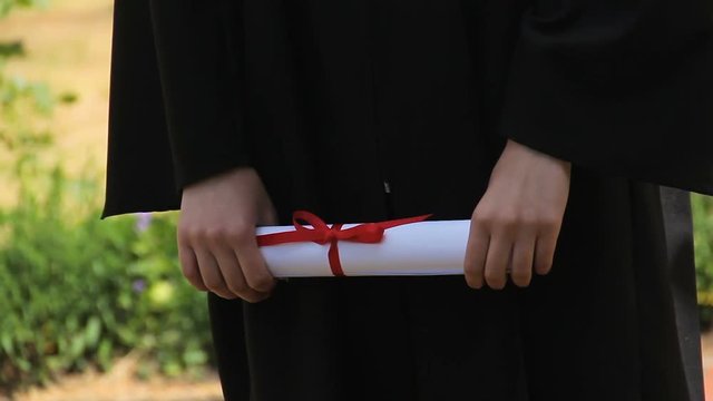 Hands of graduate holding diploma certificate tied with red ribbon, graduation