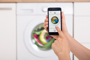 Woman Using Mobile Phone To Operate Washing Machine