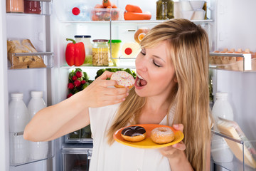 Woman Eating Sweet Donut Near Refrigerator