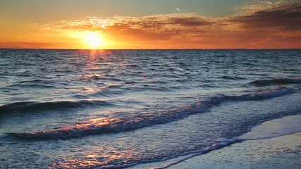 Looping video features a beautiful scene with the setting sun painting the sky above waves breaking gently on a sandy Florida Beach at Lover Key. - Powered by Adobe