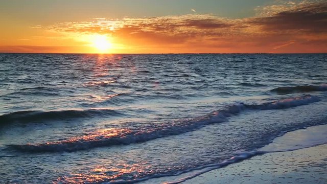 Looping video features a beautiful scene with the setting sun painting the sky above waves breaking gently on a sandy Florida Beach at Lover Key.