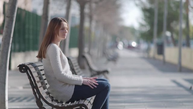 Woman sitting in a bench at the park. She looks upside and enjoys the warm sun.