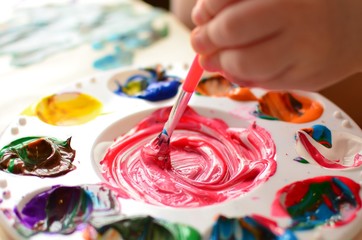 Fototapeta premium Child mixing paint on a palette of colorful paint