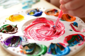 Child mixing paint on a palette of colorful paint