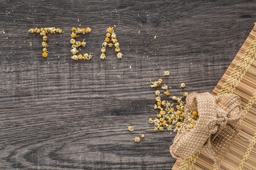 Word tea. Dried chamomile herbal tea on the wooden table as background. Healthy drink.