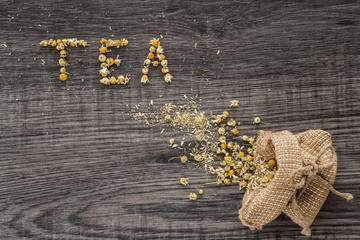 Word tea. Dried chamomile herbal tea on the wooden table as background. Healthy drink.