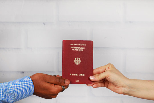 Afrikanische und europäische Hand halten einen deutschen Reisepass vor weißer Wand