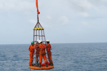 Workers are lifted by the crane to the offshore platform, Transfer crews by personal basket from the platform to crews boat © chanjaok1