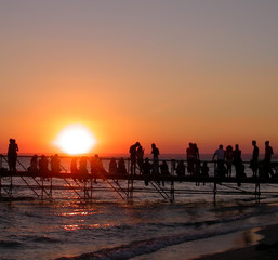 Group of young people on sea beach watching the sunset during music festival