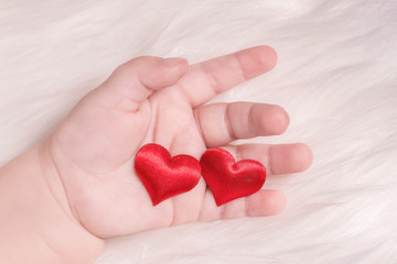 Red heart in the hand of a baby on white fur background