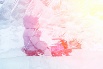 Little girl sitting on a sled behind a transparent ice in the sunlight