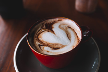 A red cup of coffee with white foam on the wooden table