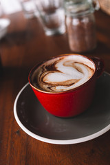 A red cup of coffee with white foam on the wooden table