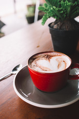 A red cup of coffee with white foam on the wooden table