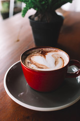 A red cup of coffee with white foam on the wooden table