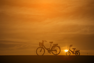 Fototapeta na wymiar Silhouette of two bike ,with bikes for adults (mother) and children.The background image is a sunset in Thailand.