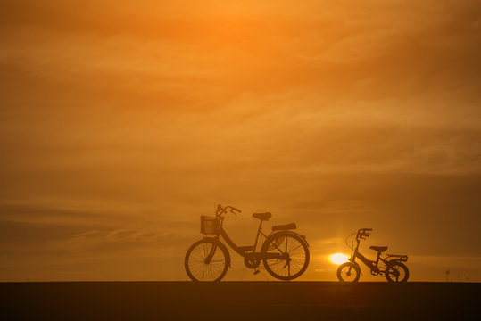 Silhouette of two bike ,with bikes for adults (mother) and children.The background image is a sunset in Thailand.