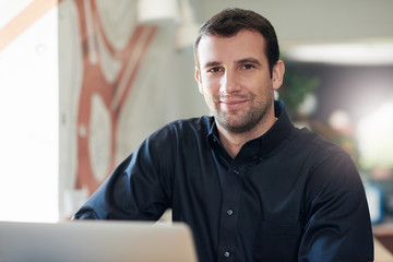 Successful businessman smiling and using a laptop in an office