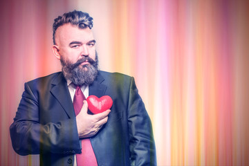 Adult bearded man in a suit holding red heart on a colorful striped background