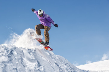Stylish snowboarder with helmet and mask jumps from high snow slope