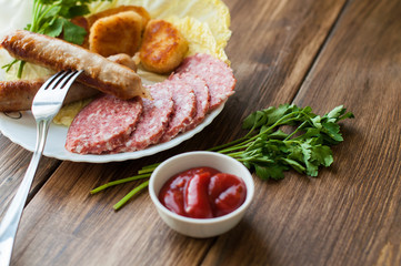 Grilled sausages and meat with vegetables and sauce on the table. On the wooden background, banner for cafe