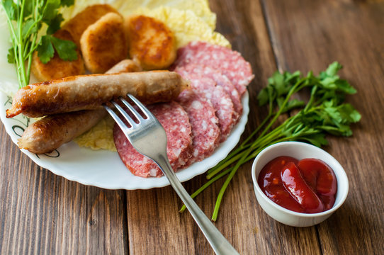 Grilled sausages and meat with vegetables and sauce on the table. On the wooden background, banner for cafe