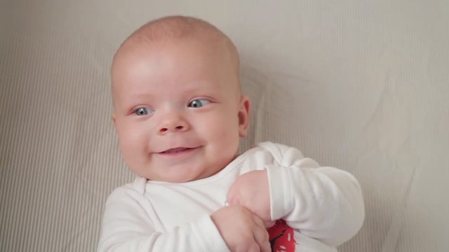 A cute little baby is looking into the camera and is happy on a white bed sheet.