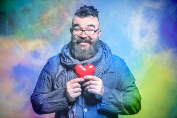 Adult bearded man in a blue jacket and scarf holding red heart  on a multicolor background