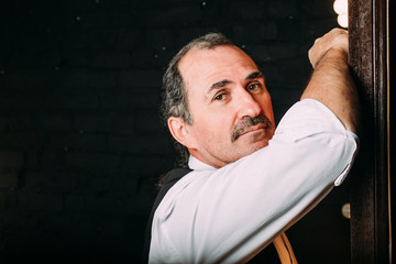 Handsome middle aged man is dressed in a white shirt and a black vest. Black background.