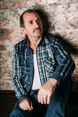 Handsome middle aged man is dressed in a casual clothing. Red brick wall background.