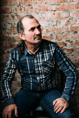 Handsome middle aged man is dressed in a casual clothing. Red brick wall background.