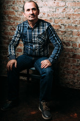 Handsome middle aged man is dressed in a casual clothing. Red brick wall background.