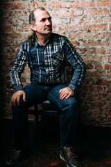 Handsome middle aged man is dressed in a casual clothing. Red brick wall background.