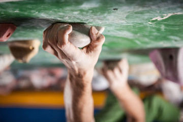 man's hands on handhold on artificial climbing wall