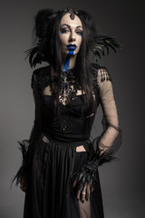 Young woman in black fantasy costume with feathers on dark background