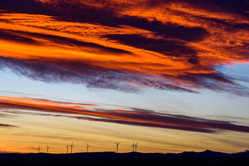 Fototapeta premium Wind Turbines Farm In The Distance On Beautiful Red, Orange And Blue Sunset