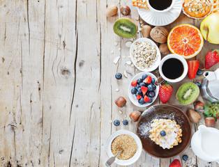 Healthy and colorful breakfast - cup of coffee with homemade granola, waffles, muffins,almond,hazelnuts,various fresh fruits, berries and milk on old wooden table.