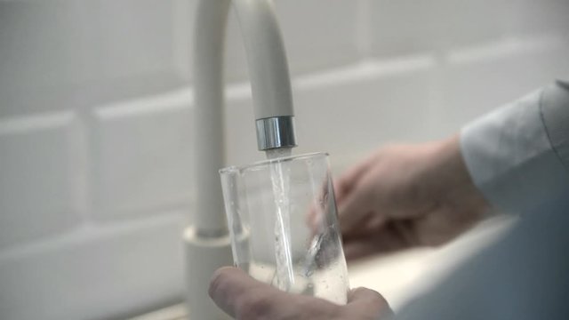 man pours water into a glass from a faucet 