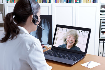 Telemedicine concept: female doctor in her surgery office with headset in front of her laptop, an...