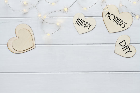 Overhead view of wooden hearts and fairy lights with message Happy Mother's Day over a flat wood table top background with copy space available.