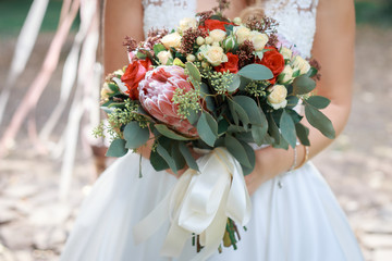 Big luxury rustic bridal bouquet with large flower and white ribbons in hands of the bride